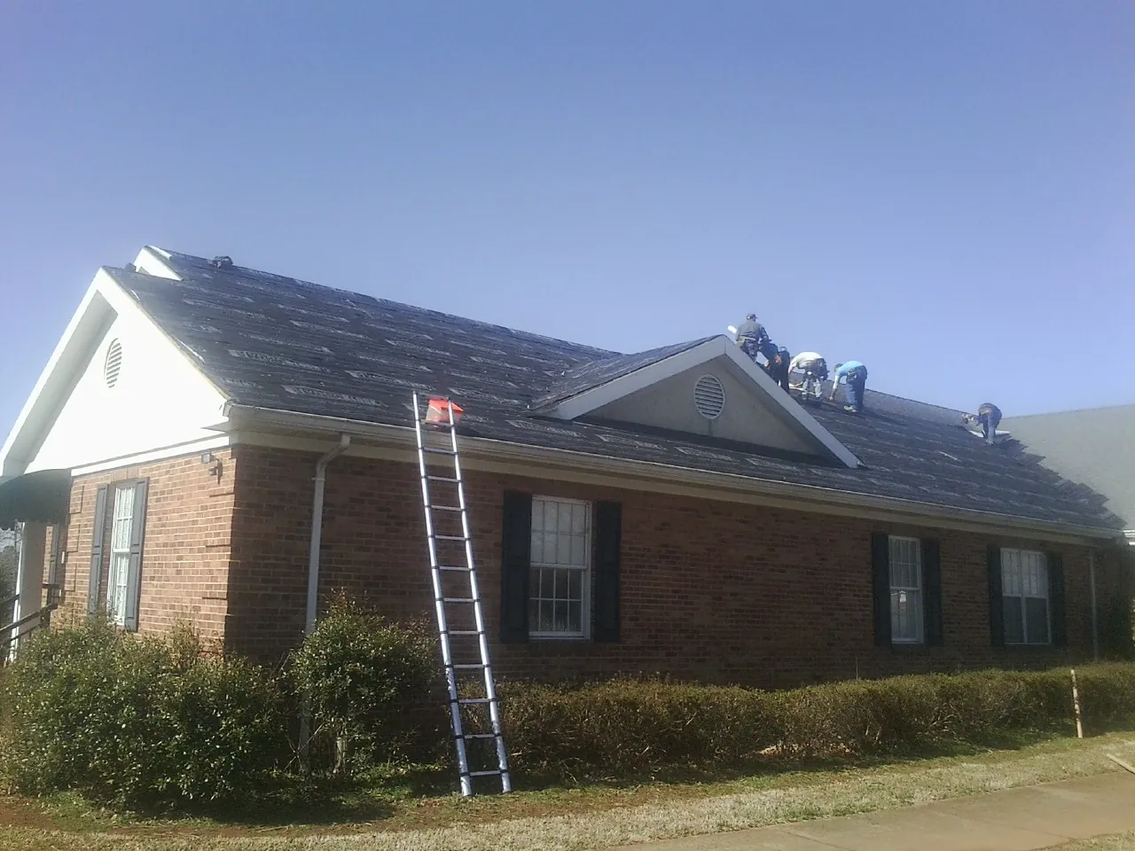 Crew tearing shingles off a brick ranch roof with a ladder set — Metal Roof Repair work by our crew in Pompton Lakes