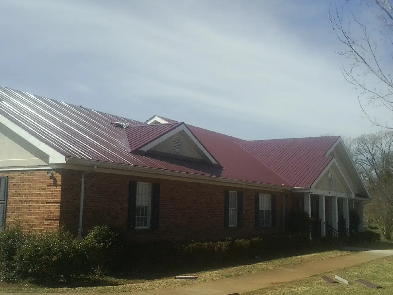 Red metal roof with gabled entries on a long brick building, from a Hail Damage Roof Repair job in Pompton Lakes