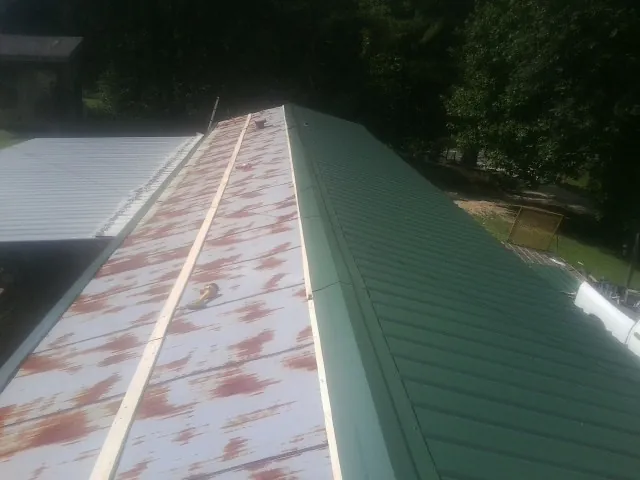 Old rusted panels beside newly installed green metal roofing — Wind Damage Roof Repair by Roofing Brothers in Pompton Lakes