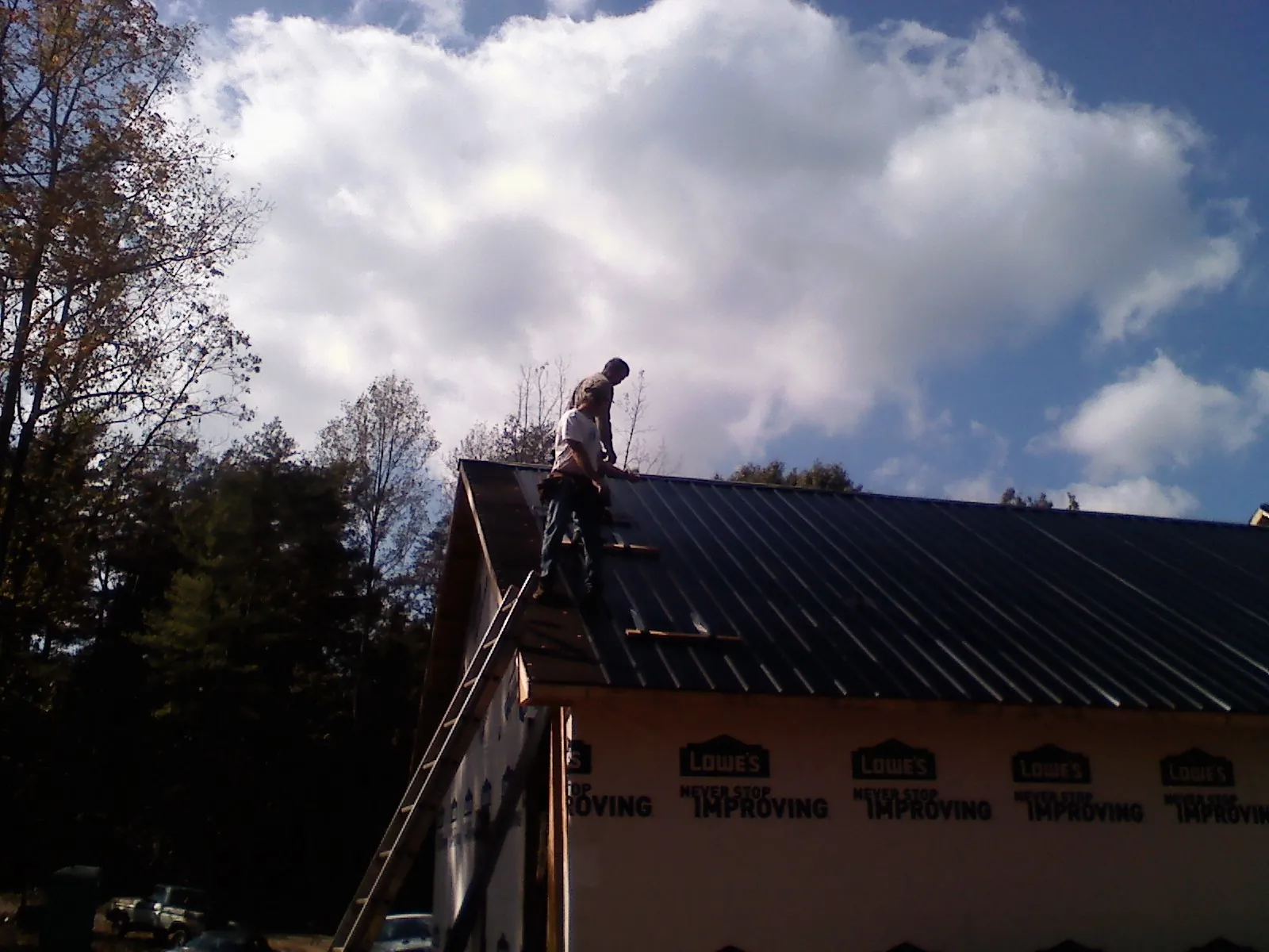 Roofer fastening dark metal panels high against a cloudy sky, from a Roof Inspection job in Pompton Lakes