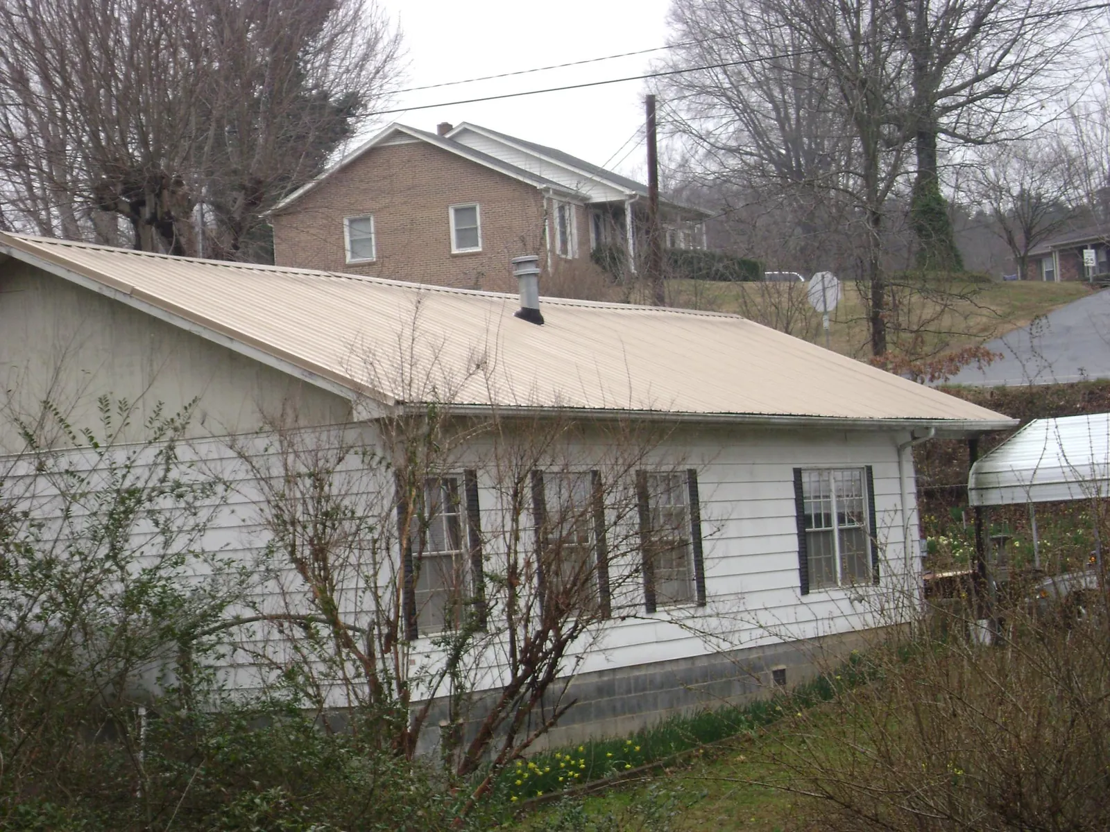 Tan metal roof on a white sided house set into a hillside — Commercial Roofing by Roofing Brothers in Pompton Lakes